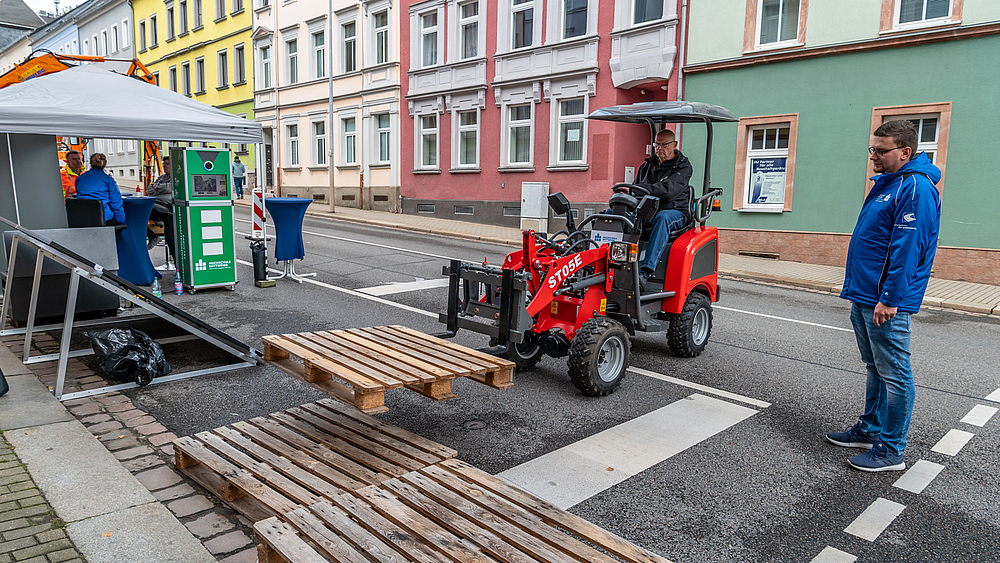 Ein kleiner roter Hoflader stapelt (durch seinen Fahrer) leere Euro-Paletten.