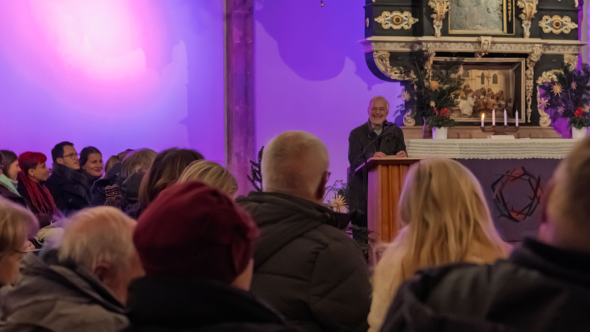 Eine männliche Person spricht lächelnd vom Pult vor dem Altar aus.