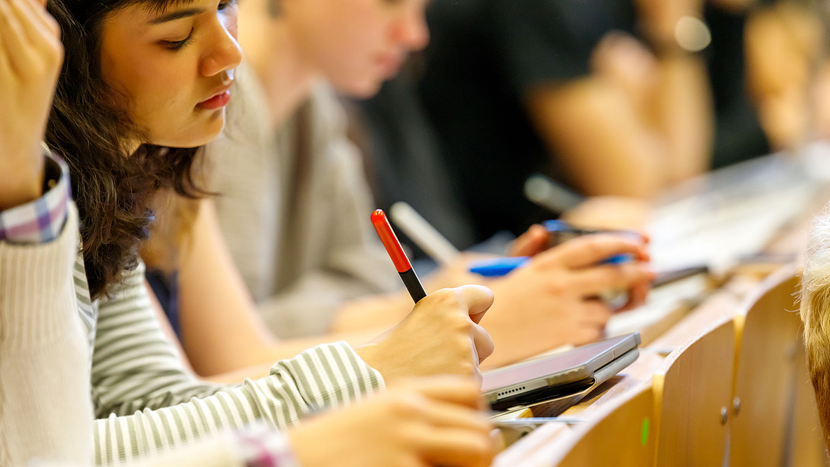 Mitschreibende Studierende in einer Bankreihe des Hörsaals.