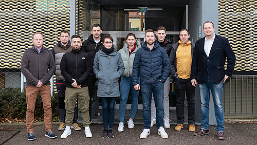 Acht männliche und zwei weiblichen Personen haben sich vor dem Eingang eines Gebäudes zum Gruppenfoto aufgestellt.