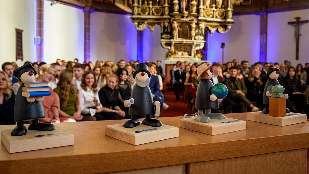 Vier verschiedene erzgebirgische Holzfiguren Willi, Charlie, Helli und Fredi stehen auf dem Rednerpult.