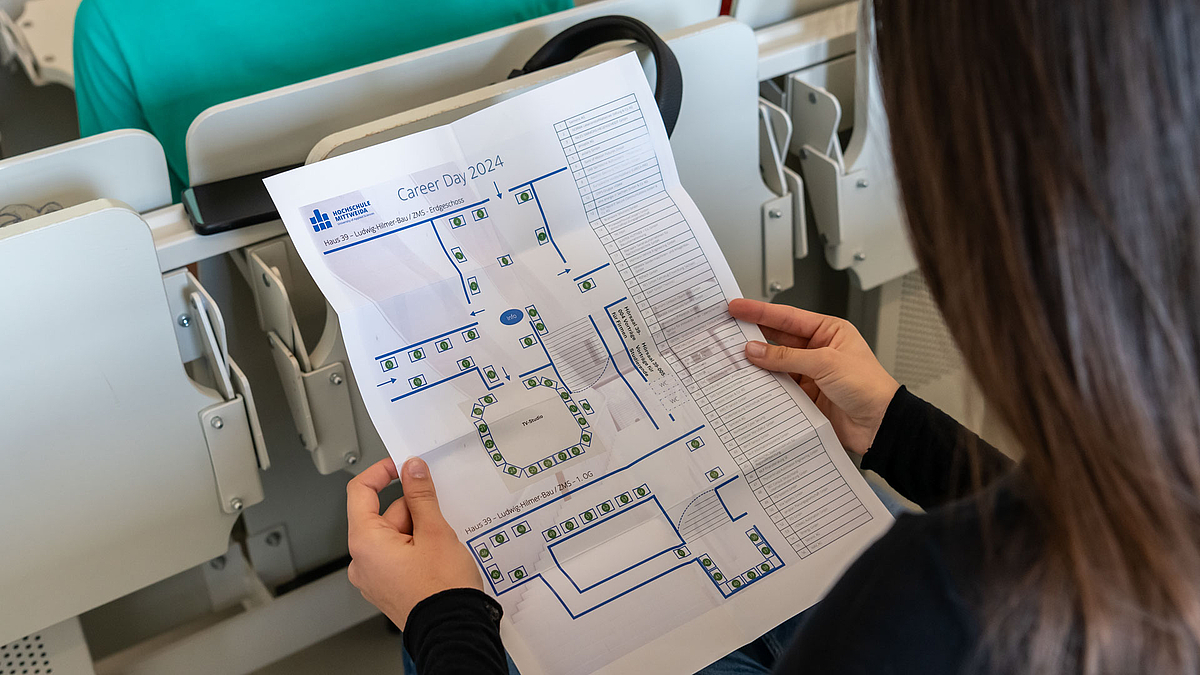 Blick von hinten auf eine weibliche Person, die sich einen Übersichtsplan vom Career Day anschaut.